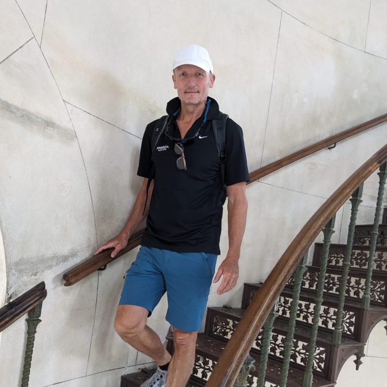 Kunde Mann in schwarzem Shirt und weißer Mütze steht an einer Treppe mit Holzgeländer.