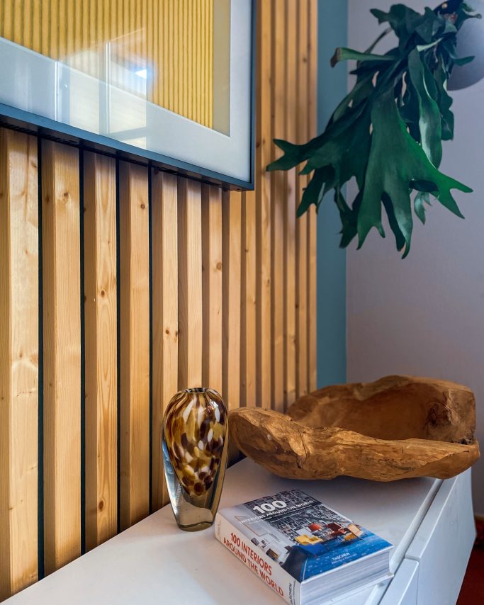 Wohnzimmer einrichten Vase und Holzschale auf einem weißen Tisch vor einer Holzvertäfelung. Gemütliches Wohnzimmer einrichten BonTemps wohnen.